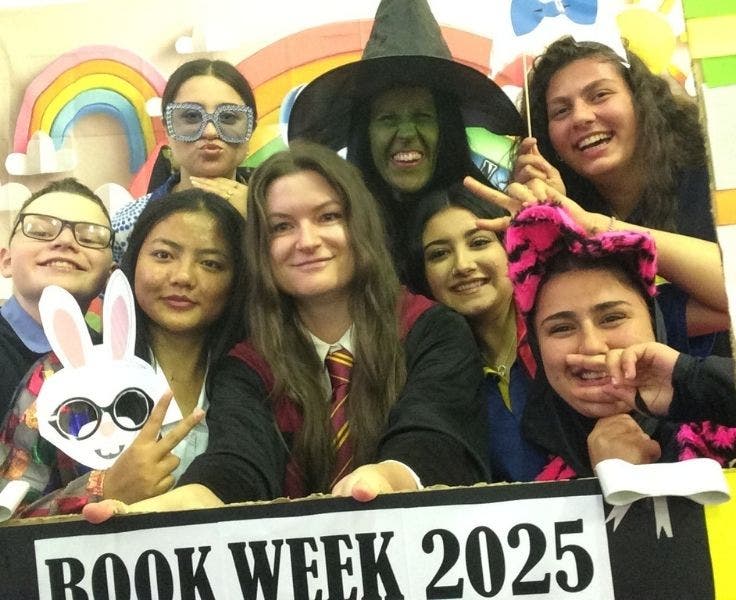 happy students with masks and hats on both sides of female teacher dressed in Harry Potter costume, with a green witch behind. celbrating book week