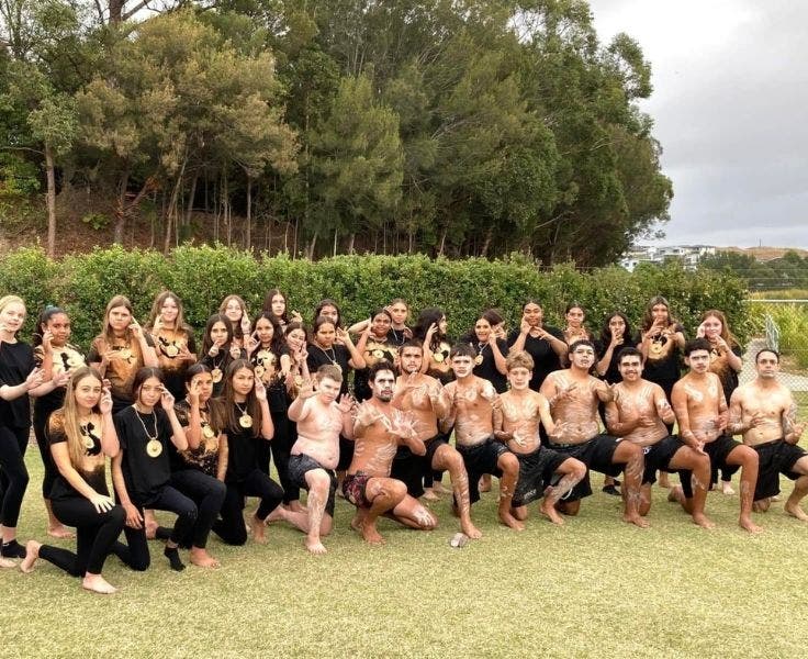 Large group of Gumbanggirr students and elders in position on bended knee with arms in dance formatiuon