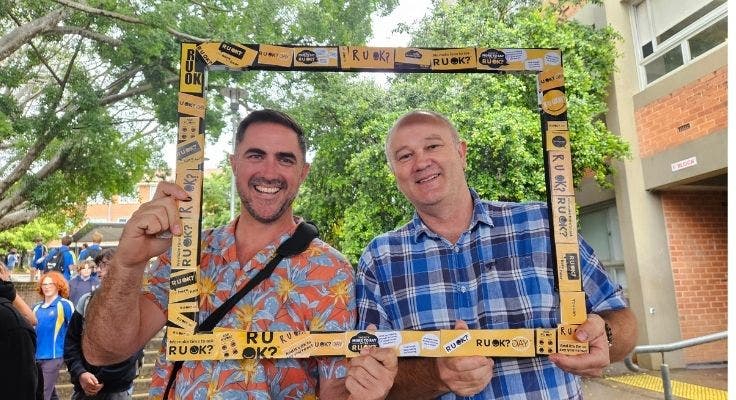 two smiling male teachers holding frame with