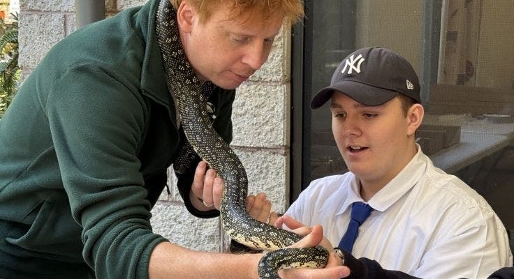teacher holding snake and student is observing and touching snake