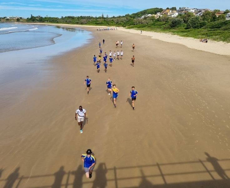 students in sports uniforms running down beach